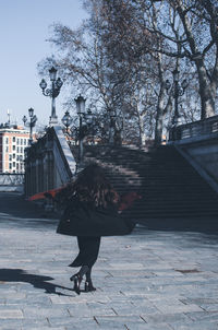 Full length of woman standing on footpath amidst buildings in city