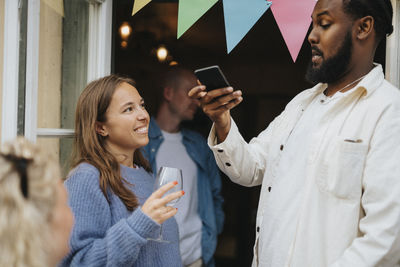 Man taking picture of female friend holding wineglass during dinner party at cafe