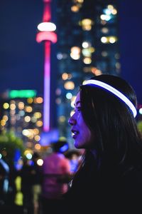 Close-up of young woman in illuminated city at night