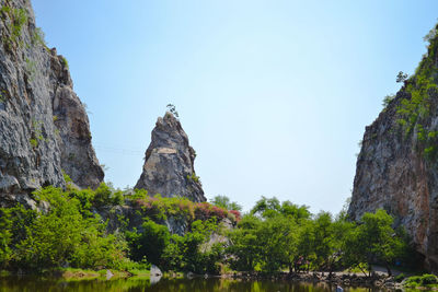 Low angle view of rocks and trees against clear sky