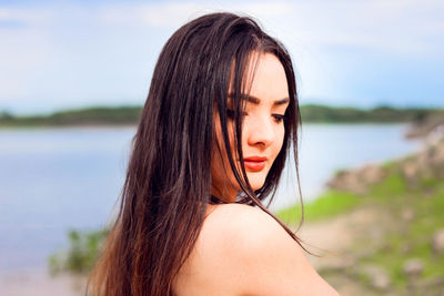 Close-up of young woman with long hair against lake