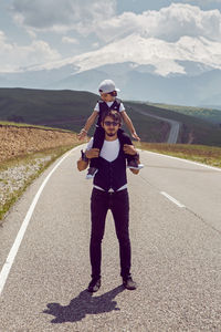 Dad and son in black vests and cap walking on the asphalt road  background of mount everest