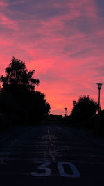 Road by silhouette trees against sky at sunset