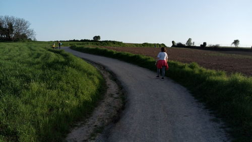 Rear view of person walking on road amidst field against sky