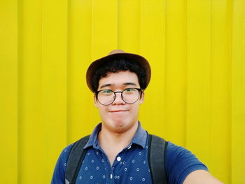 Portrait of young man wearing eyeglasses against yellow all