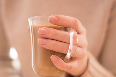 Hot coffee with milk in a transparent glass in female hands, on a biege background.