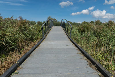 Footbridge amidst trees on field against sky