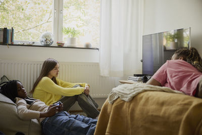 Teenage girl playing video game by female friends in bedroom at home