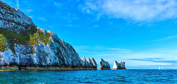 Panoramic view of cliff by sea against blue sky