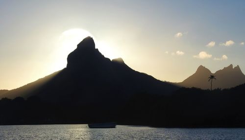 Silhouette mountain by sea against sky during sunset