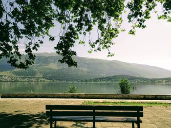 Bench by lake against sky