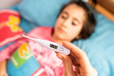 Close-up of woman hand holding thermometer over daughter lying on bed
