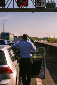 Rear view of man standing on car against sky