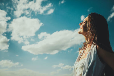 Low angle view of smiling young woman standing against cloudy sky