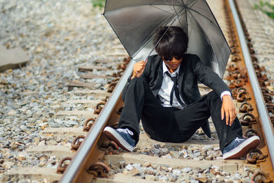 Businessman with umbrella sitting on railroad track