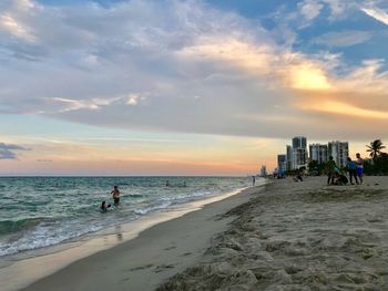 People on beach against sky during sunset