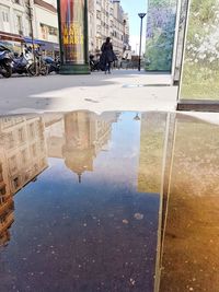 Reflection of woman sitting on puddle in city