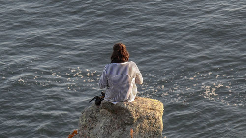 Rear view of woman sitting on rock by sea