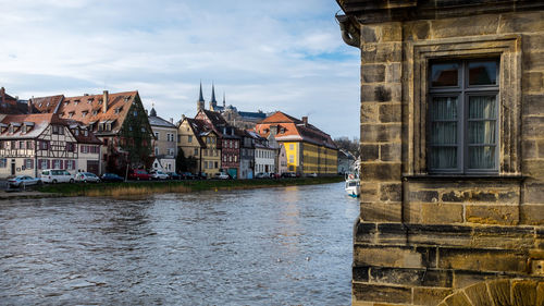 Buildings by river against cloudy sky