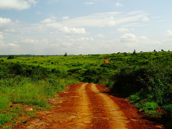 Dirt road amidst field against sky