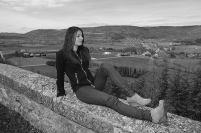 Young woman sitting on mountain against sky