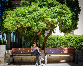 Woman sitting by tree against plants