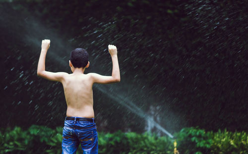 Rear view of shirtless boy standing in water