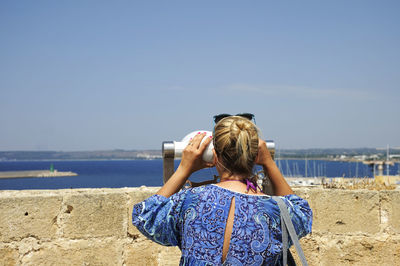 Rear view of woman looking sea through coin-operated binoculars