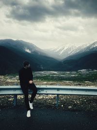 Man sitting on railing against mountains during winter