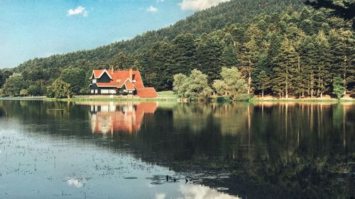 Scenic view of lake by trees and houses against sky