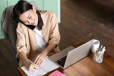 Young woman using mobile phone while sitting on table