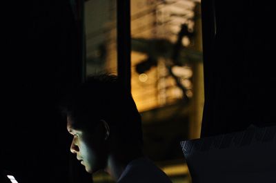 Portrait of a young man looking through window at home