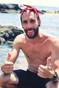 Portrait of man with starfishes on head gesturing thumbs up at beach