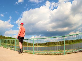 Rear view of man standing by railing against sky