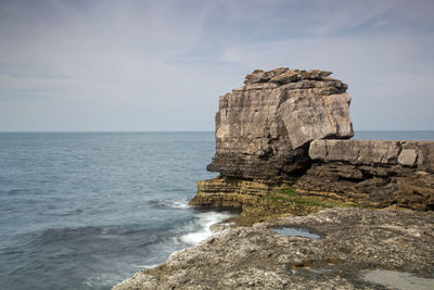 Rock formation on sea shore against sky