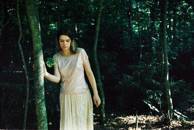 Young woman standing by tree trunk in forest