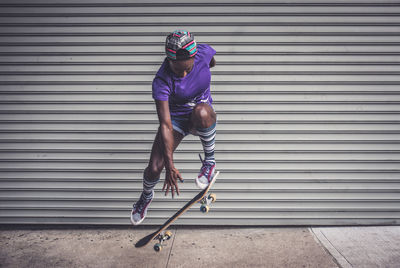 Full length of woman skateboarding against shutter