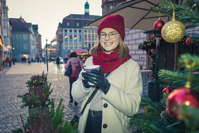 Portrait of smiling woman holding drink on street in city during christmas