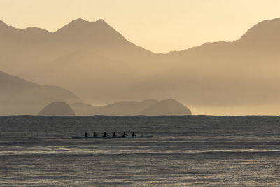 Silhouette people on boat in sea against sky during sunset