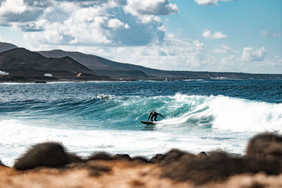 Rear view of man surfing in sea against sky