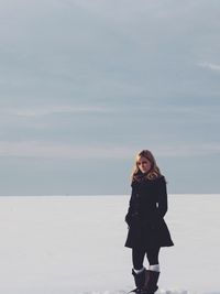 Thoughtful beautiful woman standing on snow covered field against sky