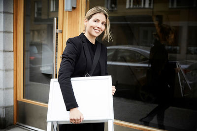 Portrait of smiling female real estate agent with blank signboard in city