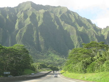 Road amidst trees and mountains against sky