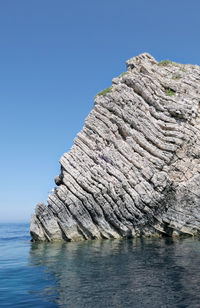 Rock formation in sea against clear blue sky