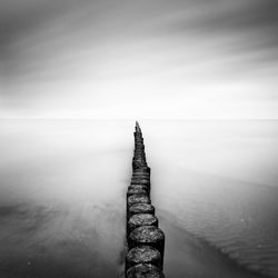 Wooden posts in sea against cloudy sky