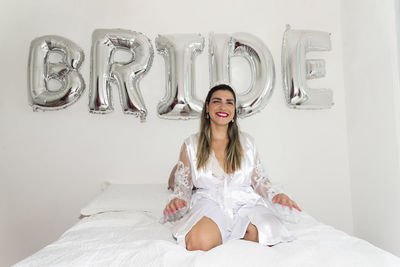 Woman sitting on bed against white wall with writing bride. 