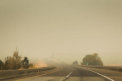 Empty road by trees against sky