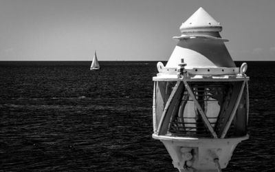 Sailboat sailing next to lighthouse on sea against sky