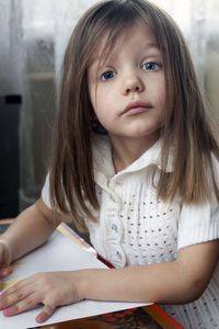 Portrait of cute girl with paper on table sitting at home