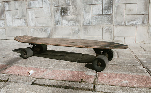 Wooden skateboard on footpath against wall